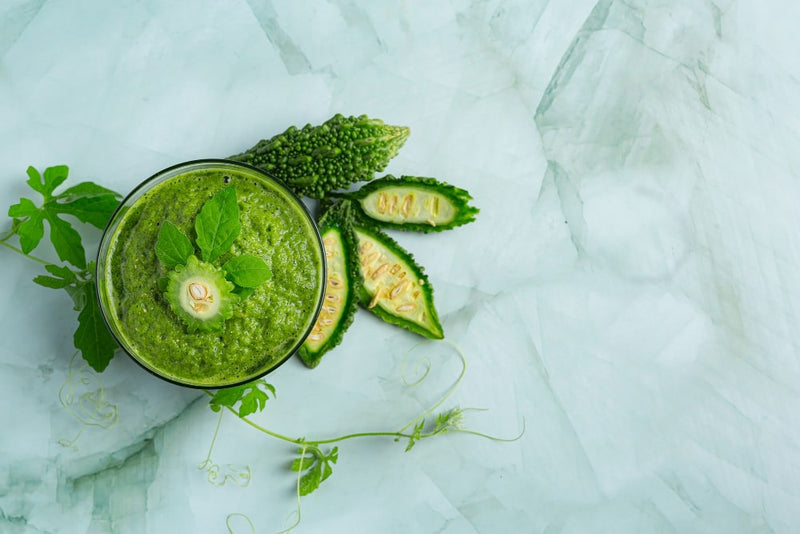 A green smoothie made with bitter melon slices, garnished with mint leaves.
