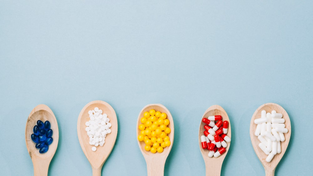 Different colored pills and supplements neatly arranged on wooden spoons.