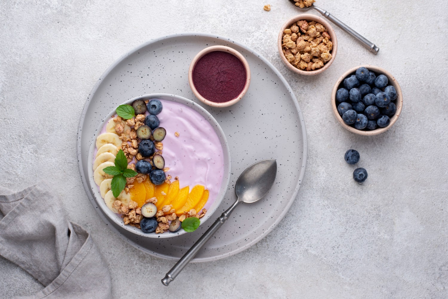 Acai yogurt bowl topped with bananas, peaches, blueberries, and granola, served with a spoon.