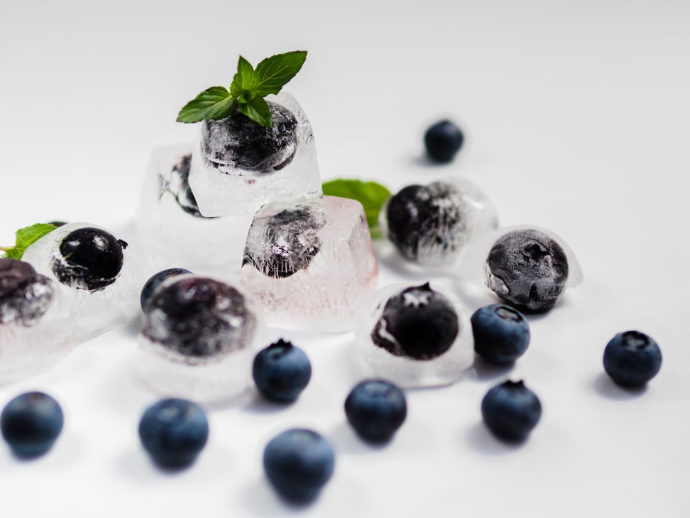 Frozen blueberries in ice cubes decorated with mint leaves on a white surface