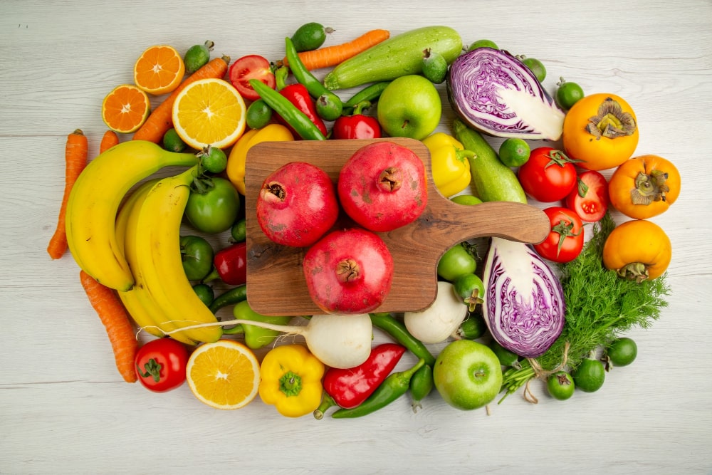 A beautiful arrangement of assorted fruits and vegetables, including bananas, pomegranates, and leafy greens