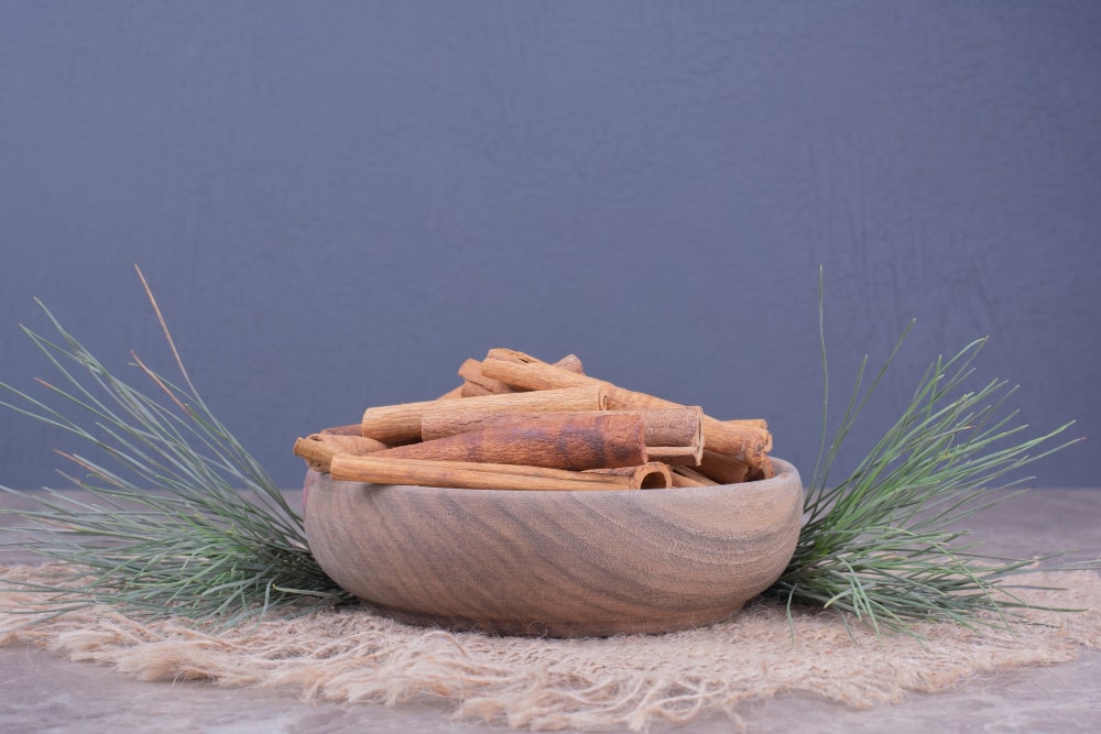 A rustic wooden bowl filled with cinnamon sticks, decorated with greenery.