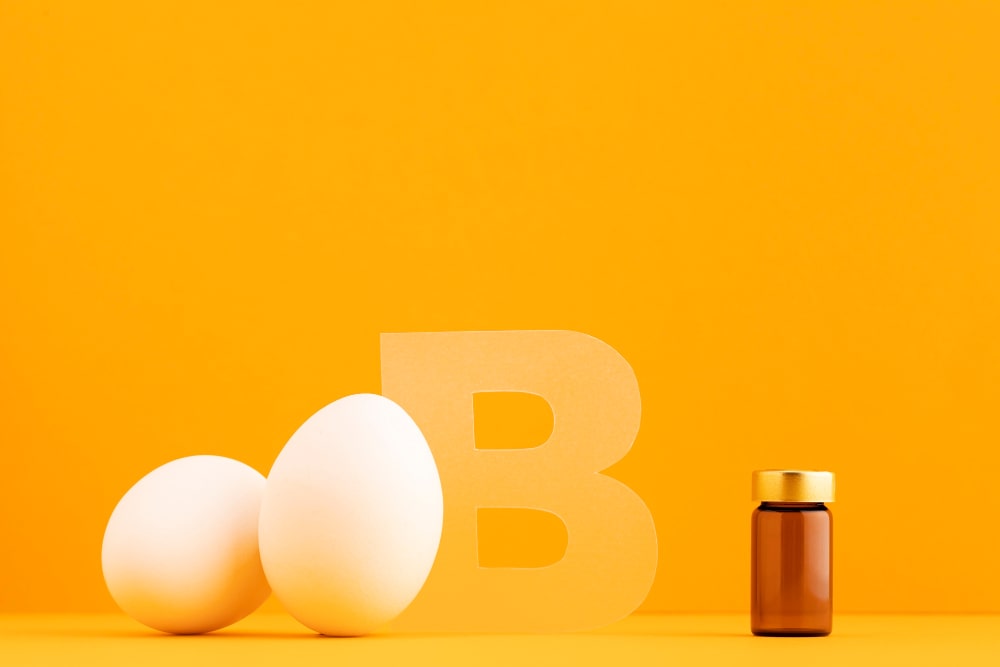 Eggs and a bottle of Vitamin B supplement against a bright orange background, highlighting the role of Vitamin B in supporting brain health and focus