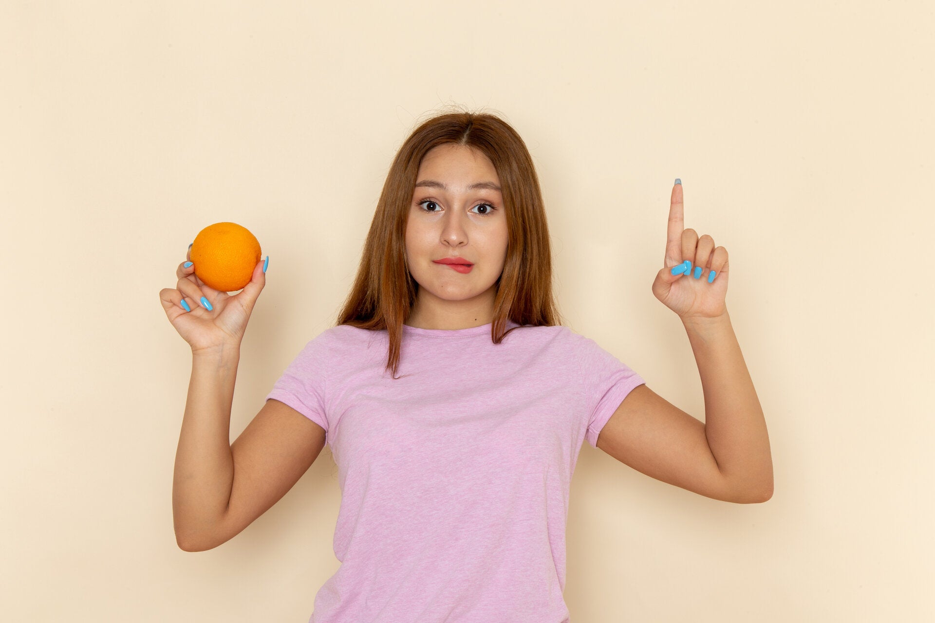 A young woman in a pink t-shirt holding an orange with a confused expression, indicating curiosity about balancing hormones.