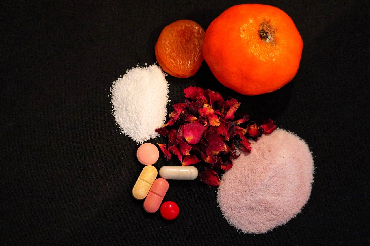 Various supplements and dried fruits displayed with a fresh orange on a black background.