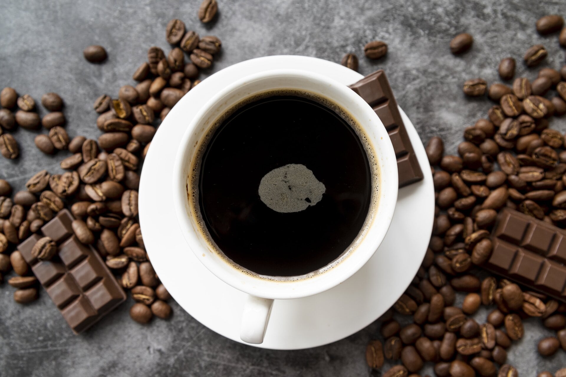 Top view of a cup of black coffee with chocolate pieces and coffee beans scattered around